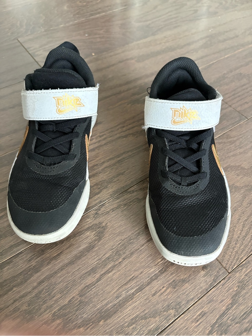 Nike’s Kids Black and White Velcro Sneakers with Gold Accent